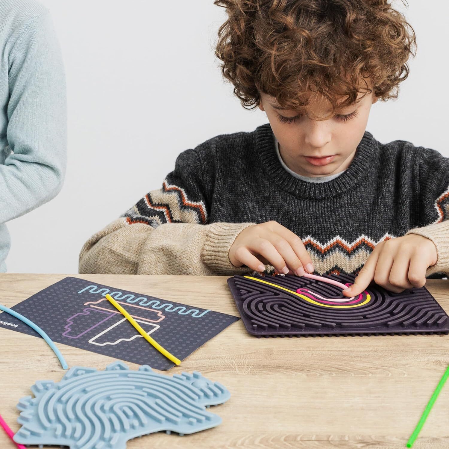 Dieťa sústredene prepletajúce pestrofarebné elastické puzzle Flexihetti Miniland na koberci